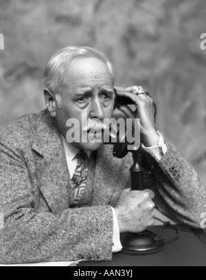 1920s 1930s ELDERLY CONCERNED WORRIED MAN TALKING ON CANDLESTICK PHONE BUSINESS MAN TWEED SUIT SERIOUS EXPRESSION Stock Photo
