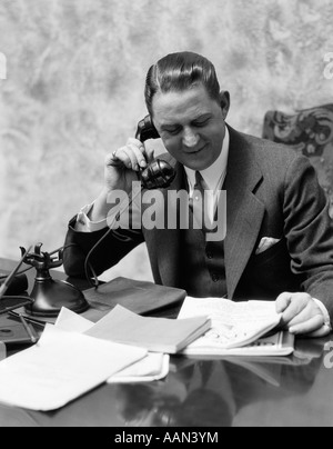 1920s 1930s MAN SITTING AT DESK TALKING ON TELEPHONE Stock Photo
