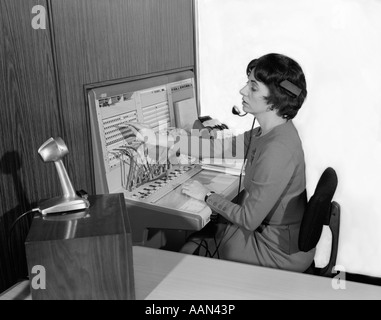 1960s WOMAN OFFICE TELEPHONE SWITCHBOARD OPERATOR WEARING HEADSET TRANSFERRING CALL RECEPTIONIST ANSWERING SERVICE MICROPHONE Stock Photo