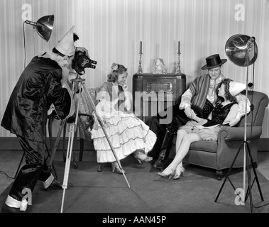 1940s COSTUMED GROUP OF TEENAGE MEN & WOMEN FILMING WITH A MOVIE CAMERA IN A LIVING ROOM WITH ARMCHAIRS AND FLOOR MODEL RADIO Stock Photo