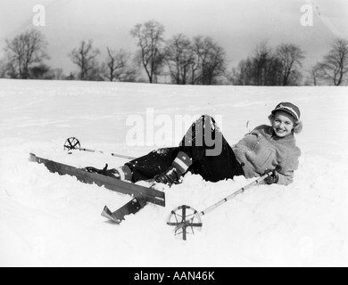 1940s 1950s SMILING WOMAN LOOKING AT CAMERA FALLEN LYING IN SNOW WITH WOOD SKIS AND BAMBOO POLES Stock Photo