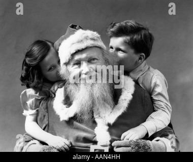 1930s MAN SMILING SANTA CLAUS POSING WITH BOY AND GIRL WHISPERING IN HIS EARS Stock Photo