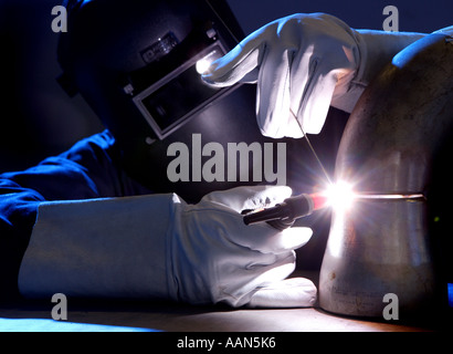 Welder welding stainless steel pipework on a work bench Stock Photo