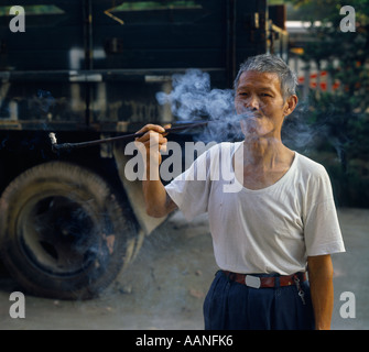 Elderly man smoking traditional pipe with long stem with old truck in background in Chongqing Sichuan China