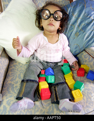 Young baby toddler aged sat on a chair with learning blocks with thick set glasses on