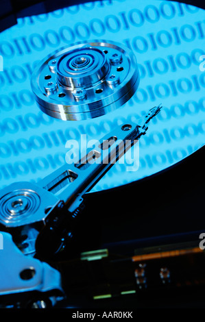 A computer hard disc exposed showing the magnetic disc platter, the read and write head and arm. Binary numbers representing the data stored on the drive are reflected on the disc platter. Stock Photo