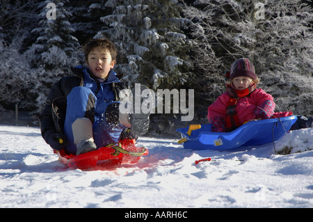 Boy and girl sledding down a snowy hill. Stock Photo