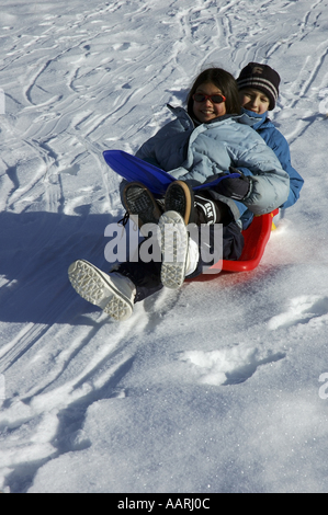 Boy and girl sledding down a snowy hill together. Stock Photo