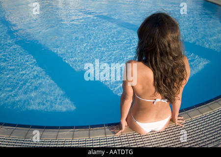 young woman sitting on edge of swimming pool Stock Photo