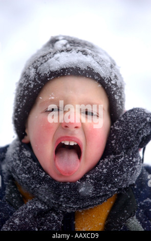 Child boy catching snowflakes on tongue as snow falls outside. 'winter weather' 'Cold Weather' concepts. Stock Photo