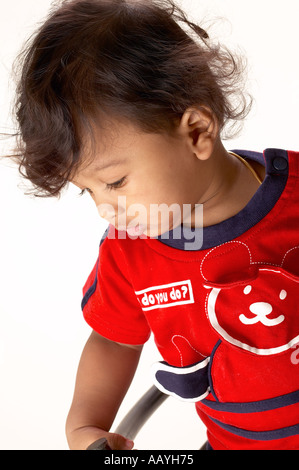 KNA70296 South Asian Indian ten months boy wearing red T shirt looking down on white background Model Release Number 631 Stock Photo