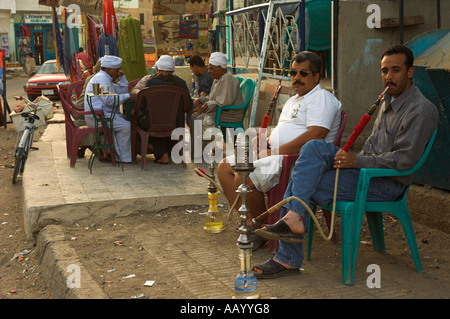 Two men sitting relaxing outside smoking shisha pipes with others around table in background El Quseir Red Sea Egypt Al Qusayr Q Stock Photo