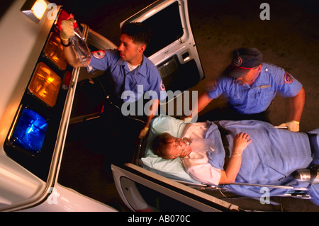 Two male emergency medical technicians with patient on gurney at rear of ambulance Stock Photo