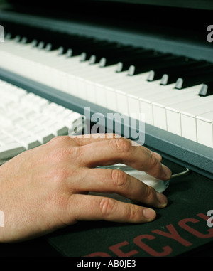 Close up of hand and mouse next to computer and musical keyboard Stock Photo