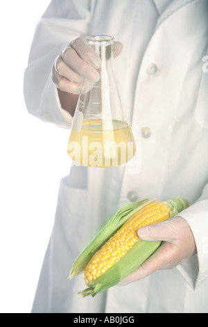 Person in lab coat holds corn and beaker of liquid Stock Photo