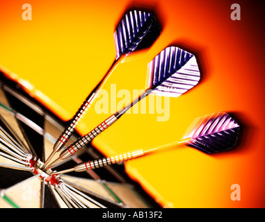 darts stuck in dartboard orange background Stock Photo