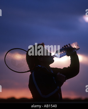 tennis player drinking water at sunset Stock Photo