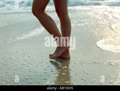 Slender beautiful legs and feet of young woman walking over wet sand on beach Stock Photo