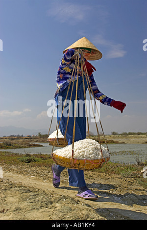 Woman in conical hat carries salt in wicker pannier baskets Phan Thiet Vietnam Stock Photo