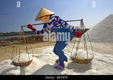 Woman in conical hat prepares to dump pannier baskets of salt on a new salt mound Vietnam Stock Photo