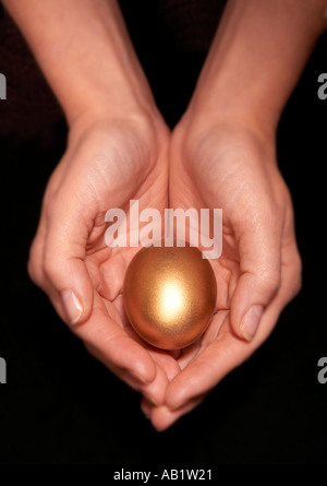 YOUNG WOMAN HOLDING GOLD EGG IN PALMS OF CUPPED HANDS Stock Photo