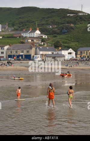 people walking in shallow water on the beach Llangrannog village Cardigan Bay Ceredigion west wales Stock Photo