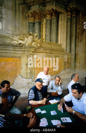 Sorrento. Italy. A group of Italian men gather to play cards against a backdrop of fading frescoes in the Sedil Dominova. Stock Photo