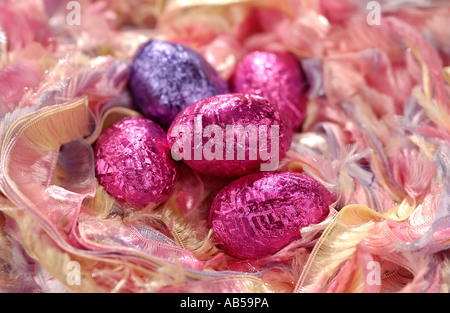 Small chocolate Easter eggs covered in colourful foil laying in a ribbon nest Stock Photo