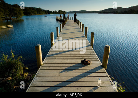 Some young couples swim and jump from a boat jetty on Lake Coniston in the late summer sunlight of the english lake district Stock Photo