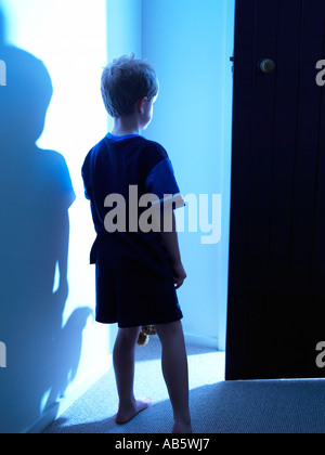 child walking in house at night going towards a blue light with anticipation dressed in pj and carrying his favorite teddy Stock Photo