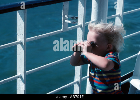 Small blond boy on a ship looking through binoculars Stock Photo