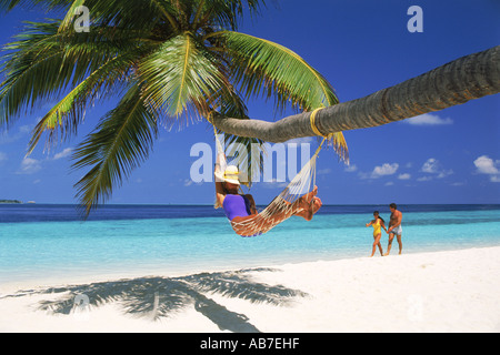 Couple passing woman in hammock over white sandy beach during tropical holidays Stock Photo