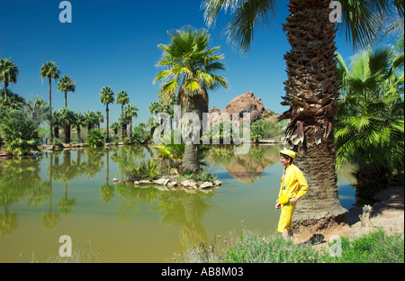 A lady dressed in bright yellow standing beside a palm oasis in Phoenix Arizona USA Stock Photo