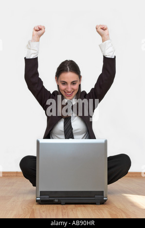 Young businesswoman sitting on floor using laptop arms raised Stock Photo