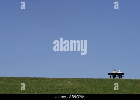 two pensioners sitting a bench on a dyke, Netherlands, Zeeland, Westkapelle Stock Photo