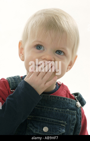 portrait of a blond boy, placing hand at his mouth. Stock Photo