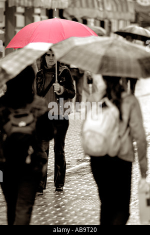Young Woman with a Red Umbrella in a Busy City Street on a Rainy Day Stock Photo