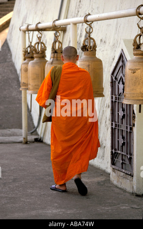 Buddhist monk walking past temple bells hanging from horizontal pole at Wat Saket, aka The Golden Mount, Bangkok, Thailand Stock Photo