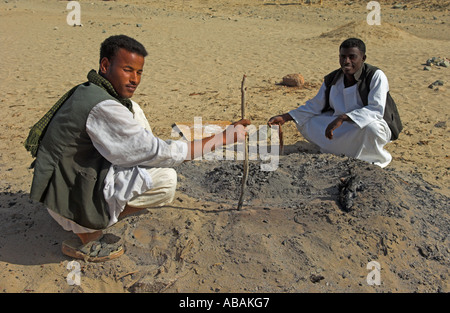 Ababda tribesman backing bread under coals from camp fire in the desert valley of Wadi El Gemal National Park Red Sea Egypt Stock Photo