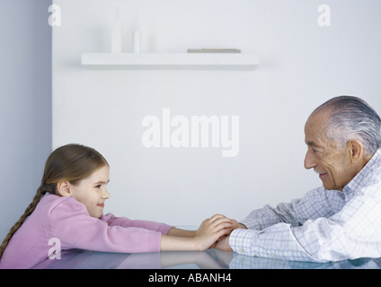 Girl and grandfather sitting across from each other at table, holding hands Stock Photo