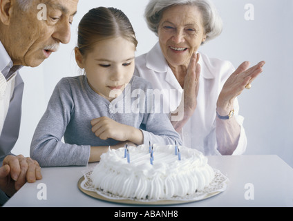 Girl with grandparents, gathered around birthday cake Stock Photo