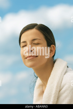 Woman wearing bathrobe, smiling with eyes closed, sky in background Stock Photo