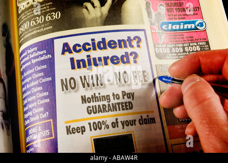 Close up of a mans hand with a yellow pages phone directory The book is open at the page listing compensation claims companies Stock Photo