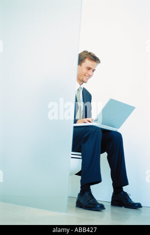 Businessman seated on toilet with laptop computer Stock Photo