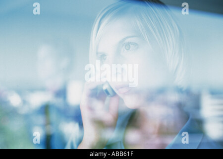 Woman using cellphone behind glass pane Stock Photo