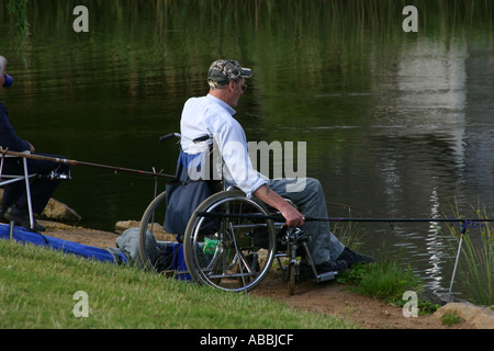 Disabled man in wheelchair on pond bank with fishing equipment enjoying the sport Stock Photo