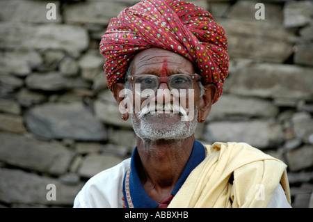 Portrait Rajpute man wearing red turban glasses and a moustache in front of ay stone wall Kelwara Rajasthan India Stock Photo