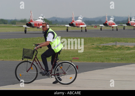 Airport groundcrew on bicycle waiting to cross ramp apron taxiway with busy aircraft taxying Stock Photo