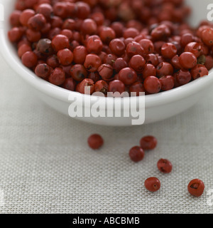 Pink peppercorns in white bowl on linen background Stock Photo