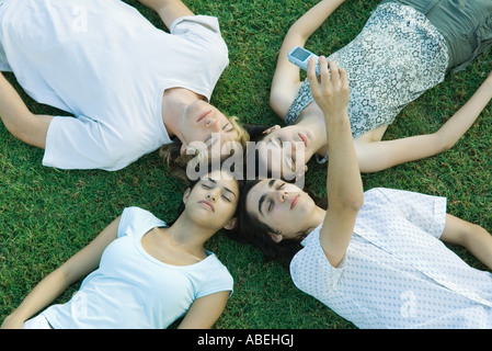 Group of young friends lying on grass with heads together, eyes closed, one taking photo with cell phone Stock Photo